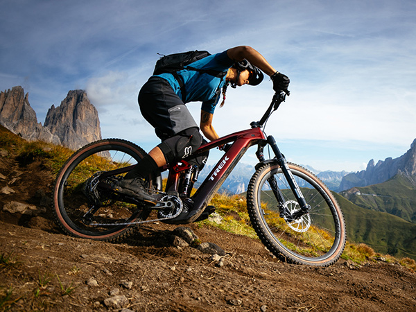 Cyclist wearing helmet while riding bike down dirt trail with mountains in background
