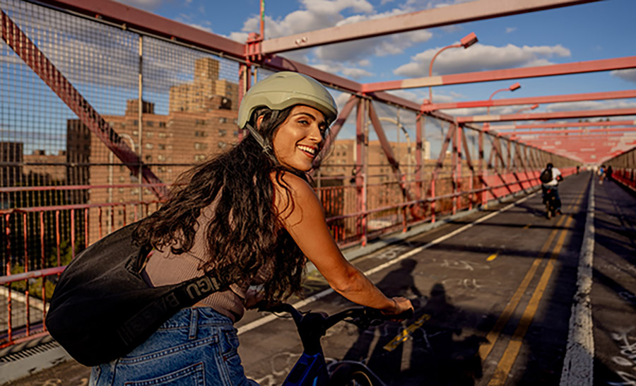 Smiling cyclist wearing helmet while riding Trek bike on paved bridge with blue and cloud-filled sky