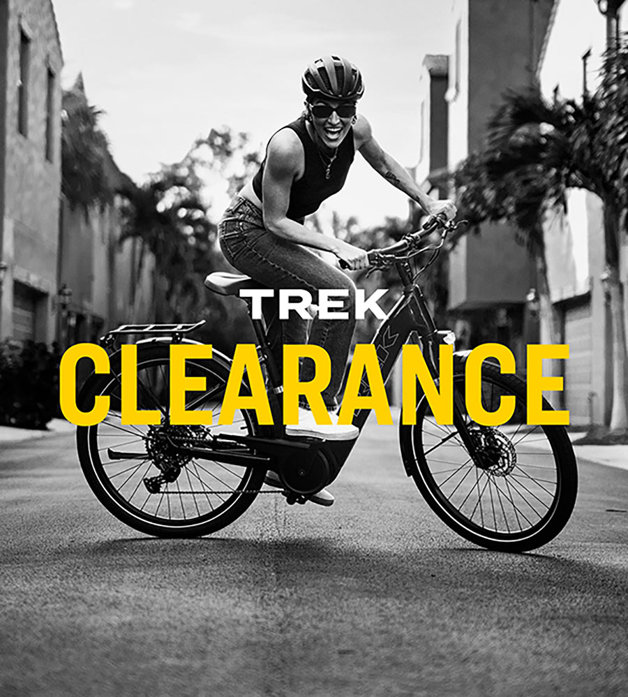 The words, 'TREK CLEARANCE' overlaying black and white photo of enthusiastic cyclist wearing helmet and sunglasses while riding bike on paved city road with buildings in background