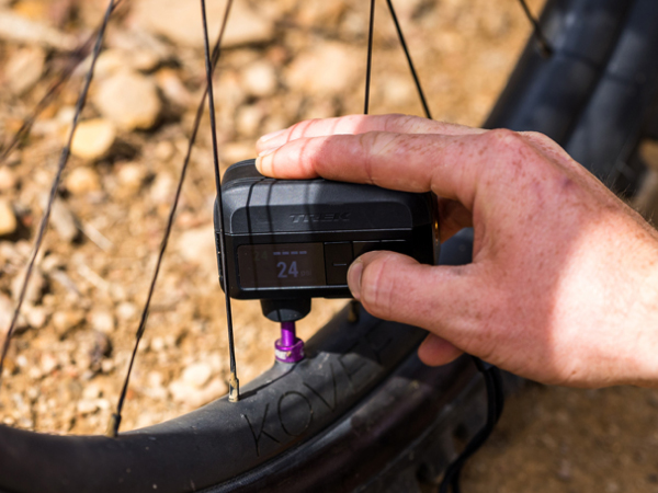 Cyclist using Trek Air Rush Electric pump to inflate bike tire with gravel in background