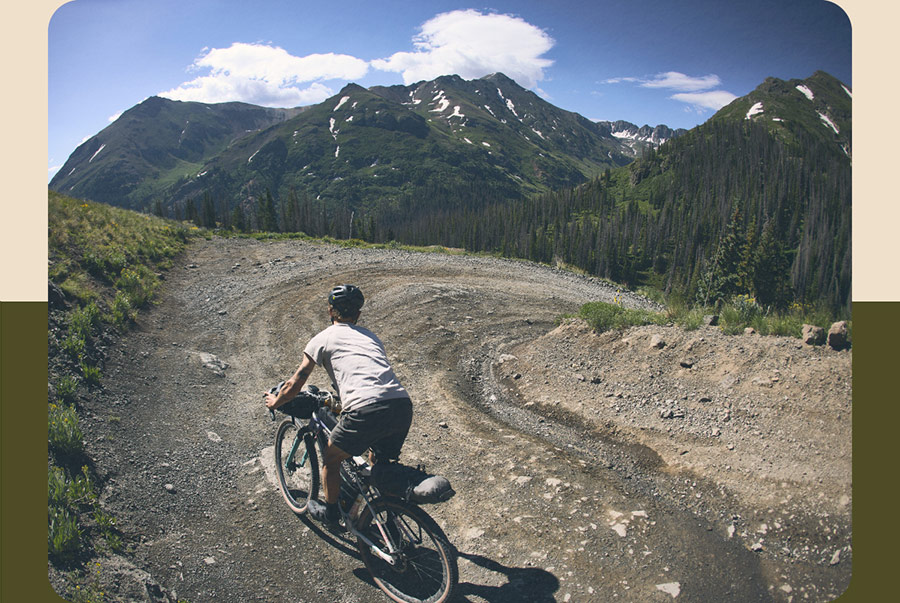 Cyclist wearing helmet while riding all-new CheckOUT bike down mountain trail with mountains in background