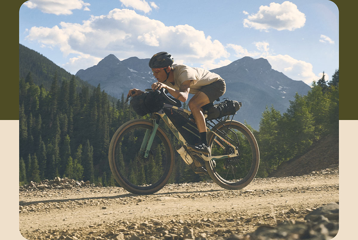 Cyclist wearing helmet while riding all-new CheckOUT bike on gravel trail with trees and mountains in background