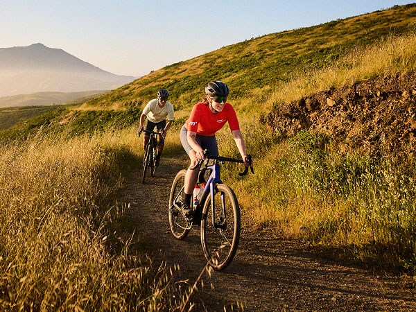 Cyclists wearing helmets while riding gravel bikes on trail with mountain in background