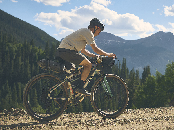 Cyclist wearing helmet while riding bike on gravel road with trees and mountains in background