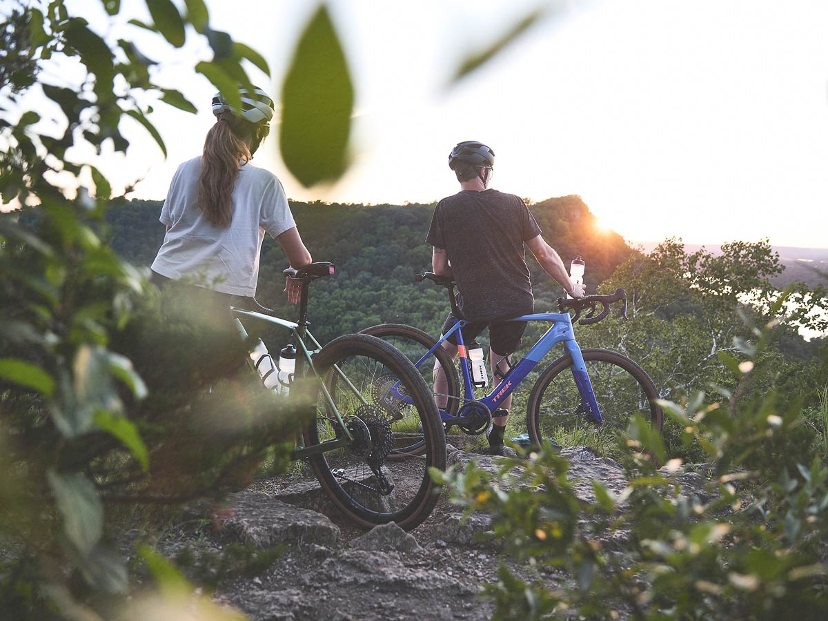 Cyclists wearing helmets while sitting on bikes and watching sun setting over trees