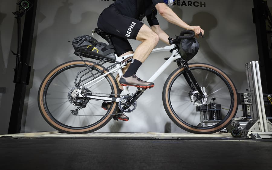 A cyclist wearing a mask rides a stationary bike in a lab while a person monitors data on computer screens at Trek Performance Research