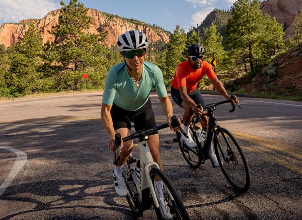 Lifestyle shot of two cyclists wearing helmets and sunglasses on road bikes
