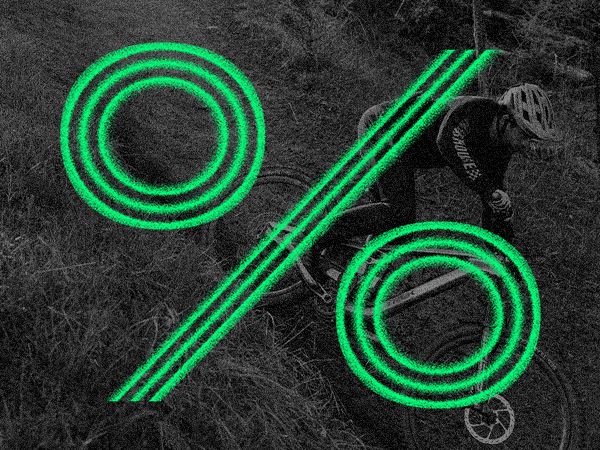 A person rides a bicycle in motion blur with a large green percentage symbol overlaying the image