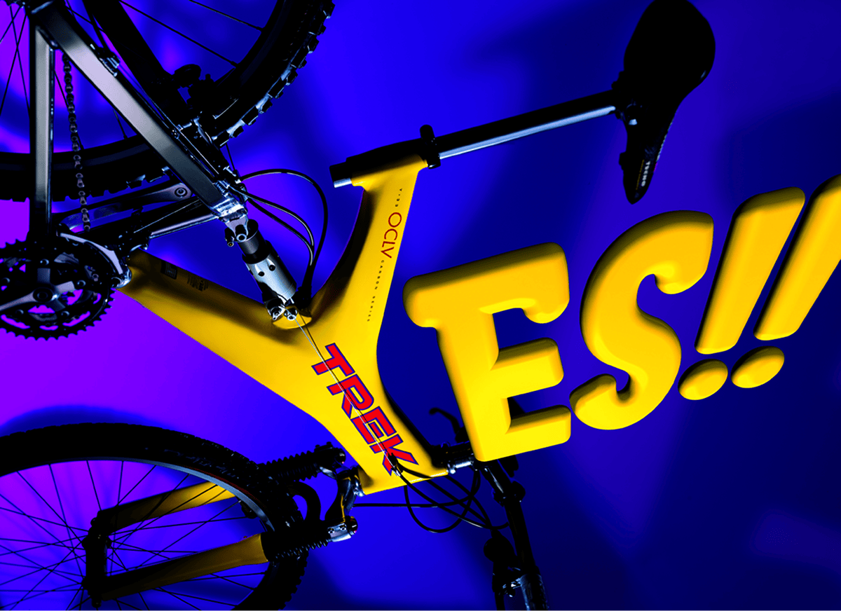 A yellow Trek bicycle with large, bold yellow letters spelling 'YES!!' partially covering the frame, set against a purple and blue background