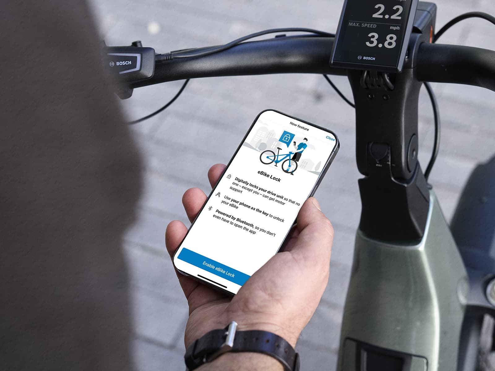 A person's hand holding a smartphone displaying the 'eBike Lock' feature on Charter+, with the bike's handlebar and display visible in the background.