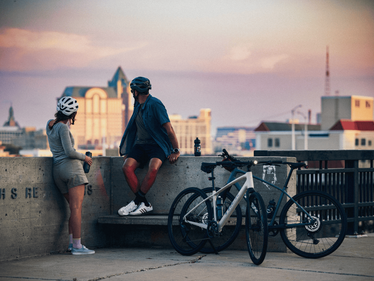 Two cyclists taking a break next to their bikes, overlooking a cityscape at sunset