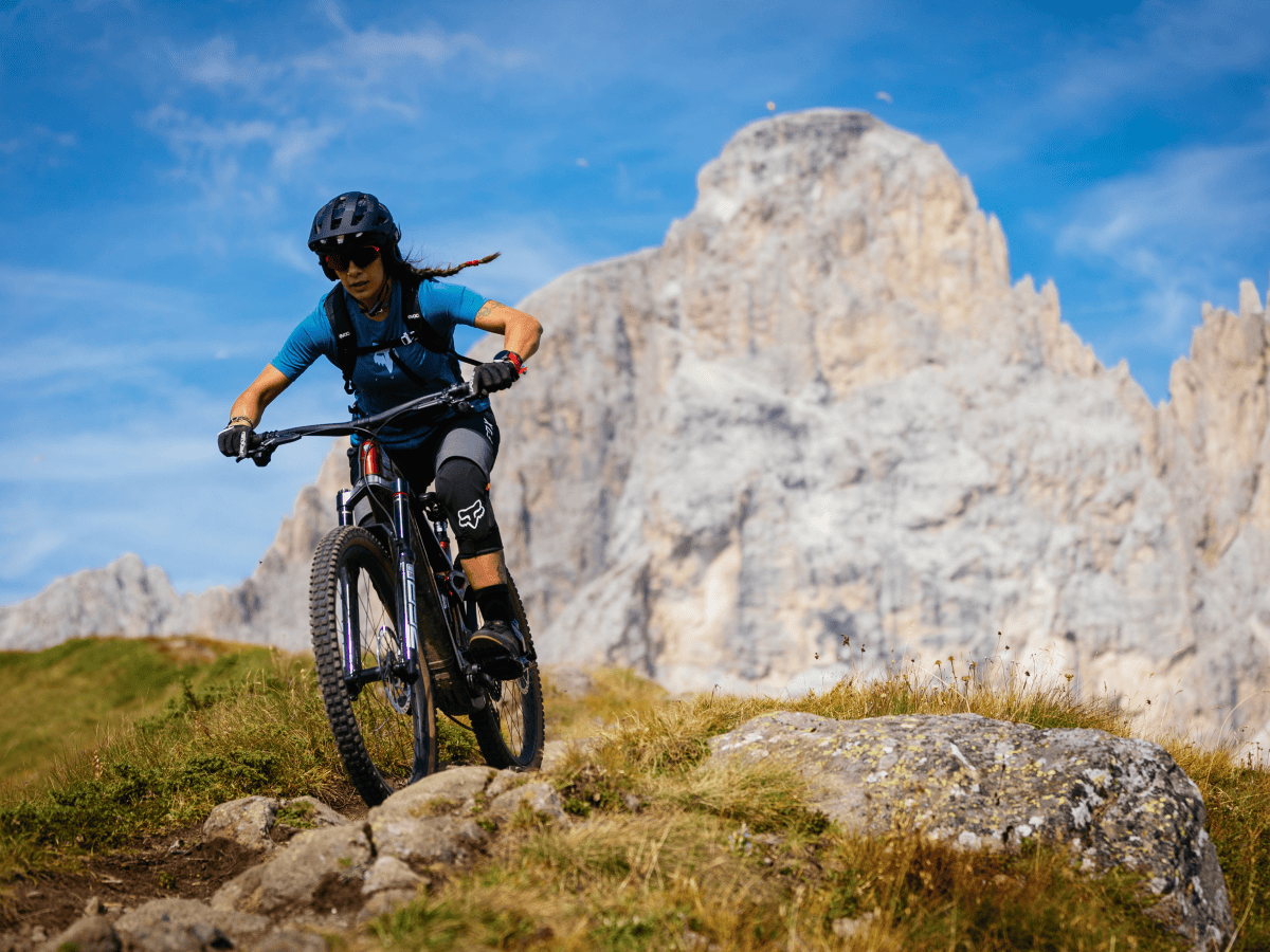 Woman riding a mountain bike on a rocky trail with a mountain backdrop