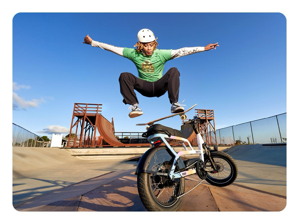 A person doing a skateboard trick, jumping over an Electra Ponto Go! electric bicycle on a skateboard ramp