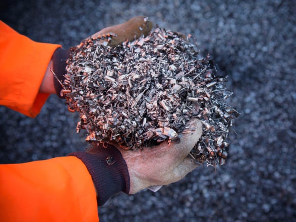 Hands wearing orange sleeves and work gloves hold a pile of metallic shavings.