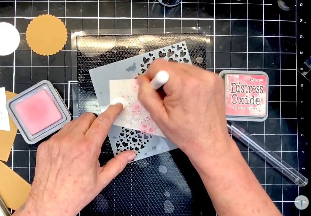Adult hands holding a blending brush and a heart stencil, inking up cardstock using the Clingy Craftmate