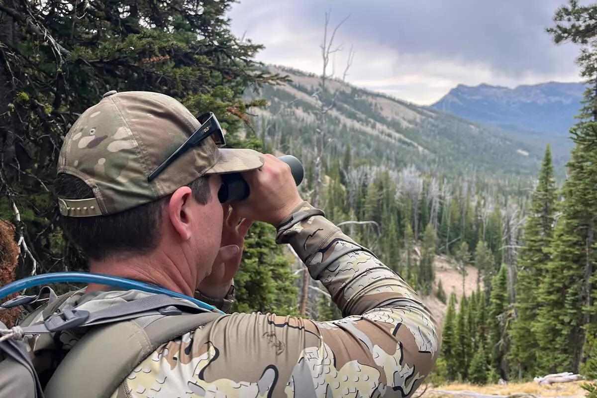 Man in camo using binoculars to observe in nature