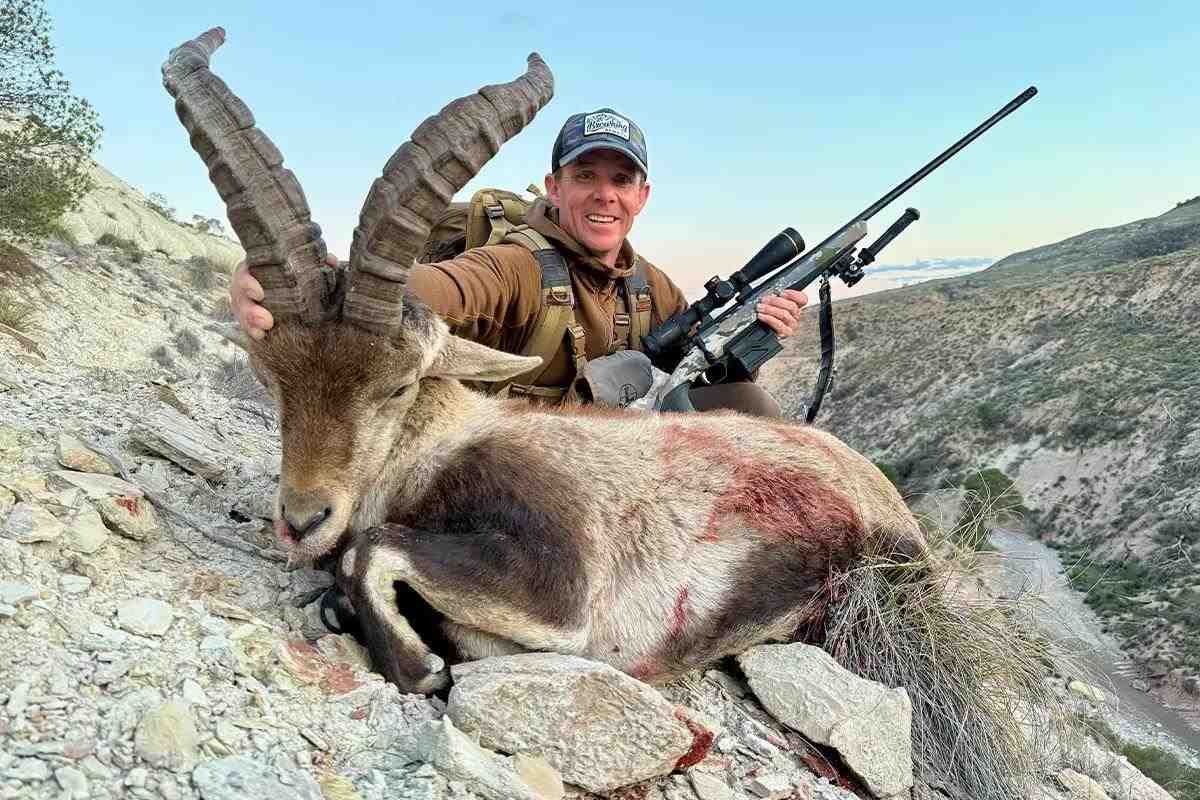 Man smiling on a mountainside behind his kill
