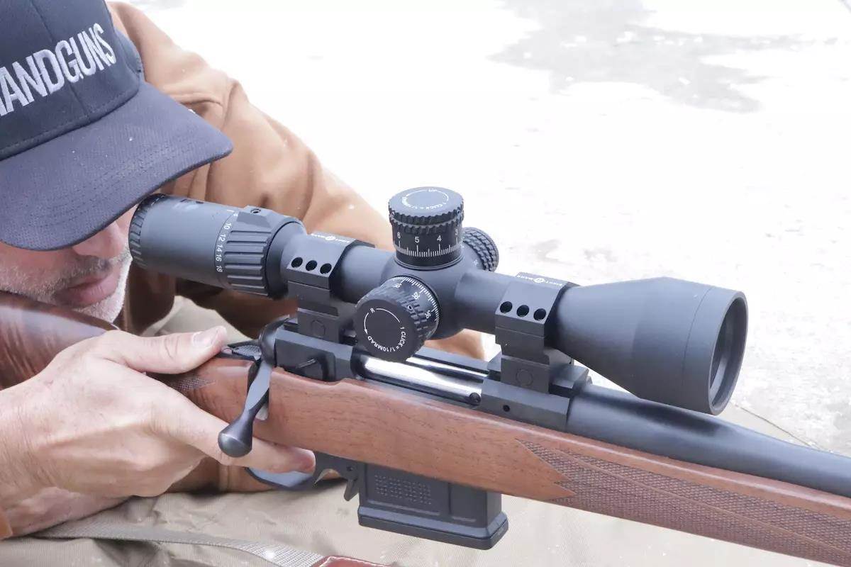 Man looking down the scope of a black and brown rifle