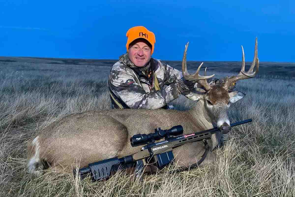Hunter leaning over freshly nabbed buck, rifle displayed in front
