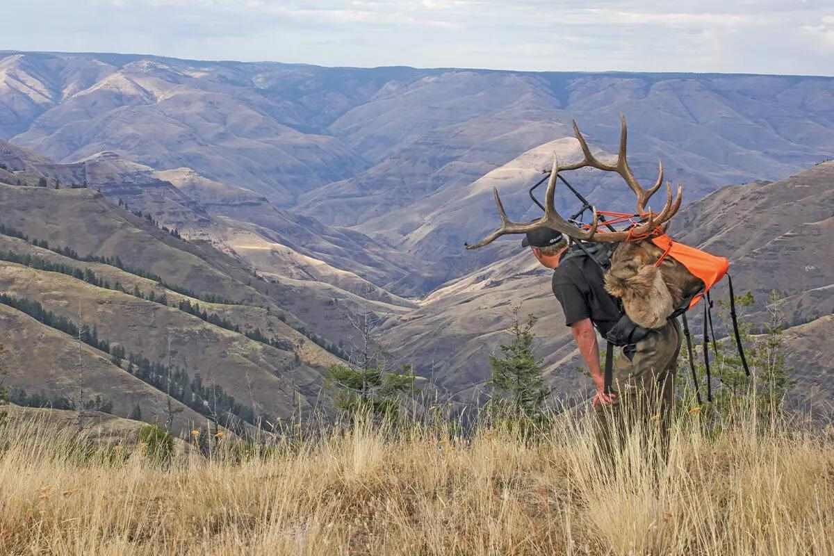 Man hiking on mountain with large shed tied to backpack