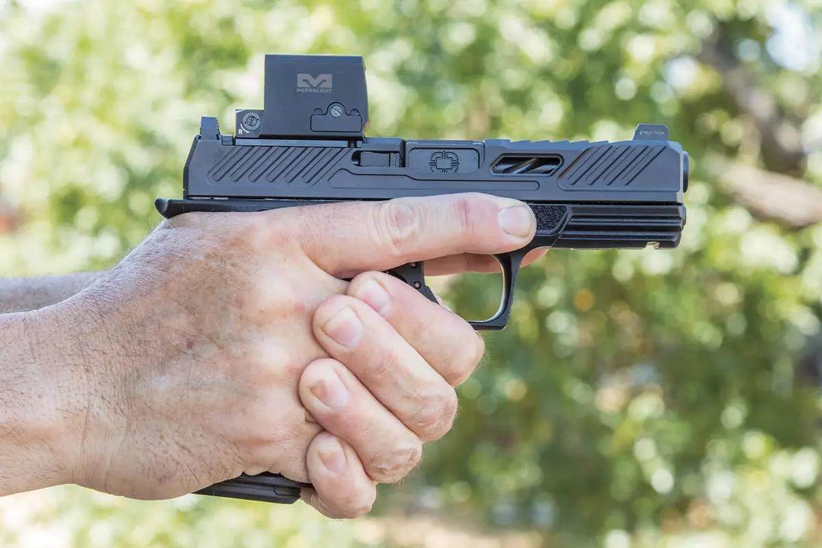 Man's hand with index finger safely along the side of a handgun, not the trigger