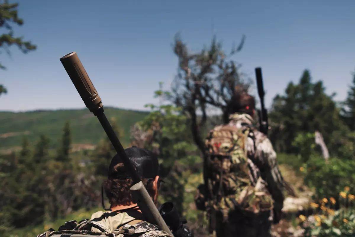 Exposed rifle barrel with suppressor, leaning on rack on mountain.