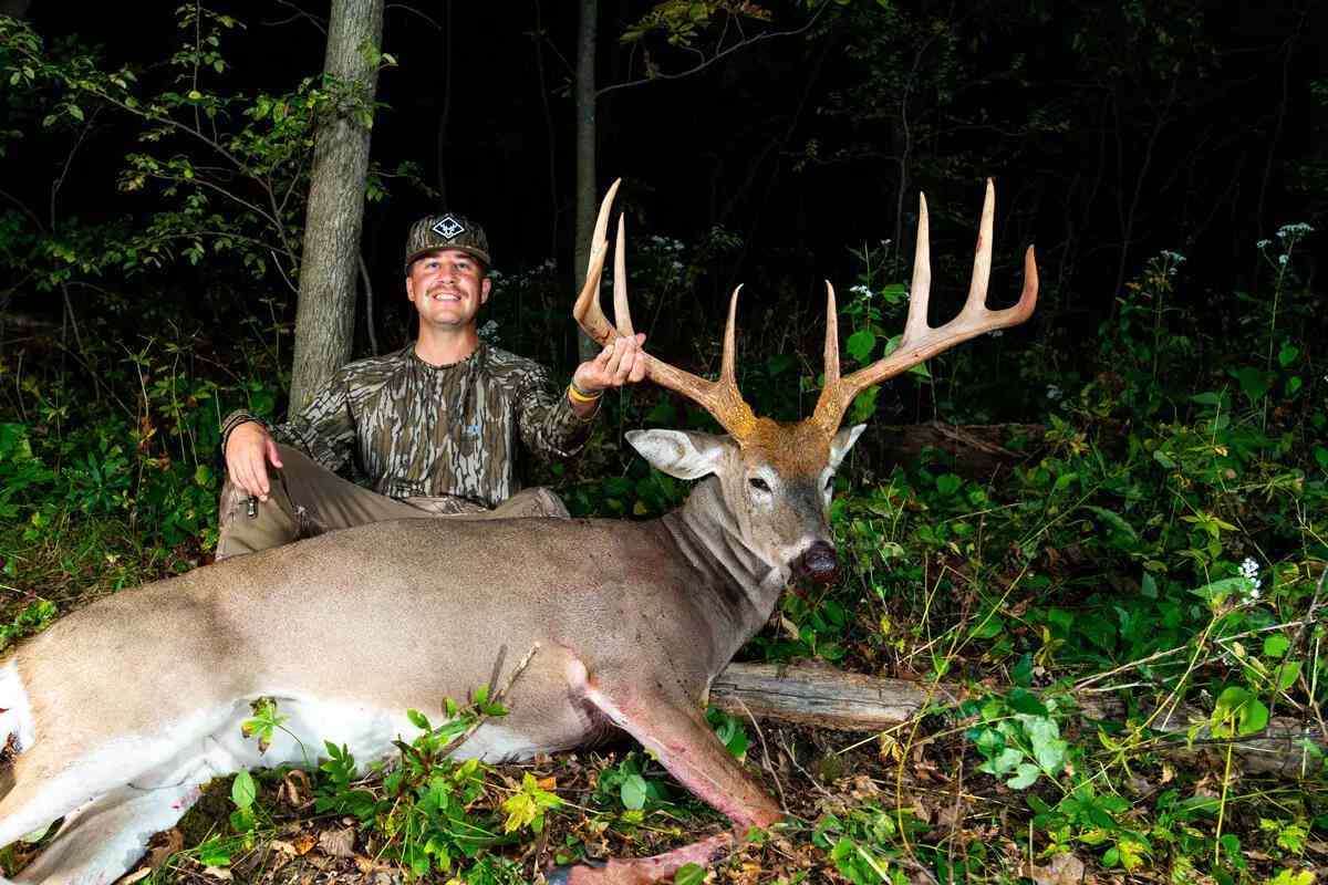 Image of man posing with large buck in woods at night