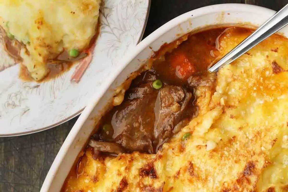 Beautifully golden-crusted cottage pie in baking dish; small portion on white plate next to it