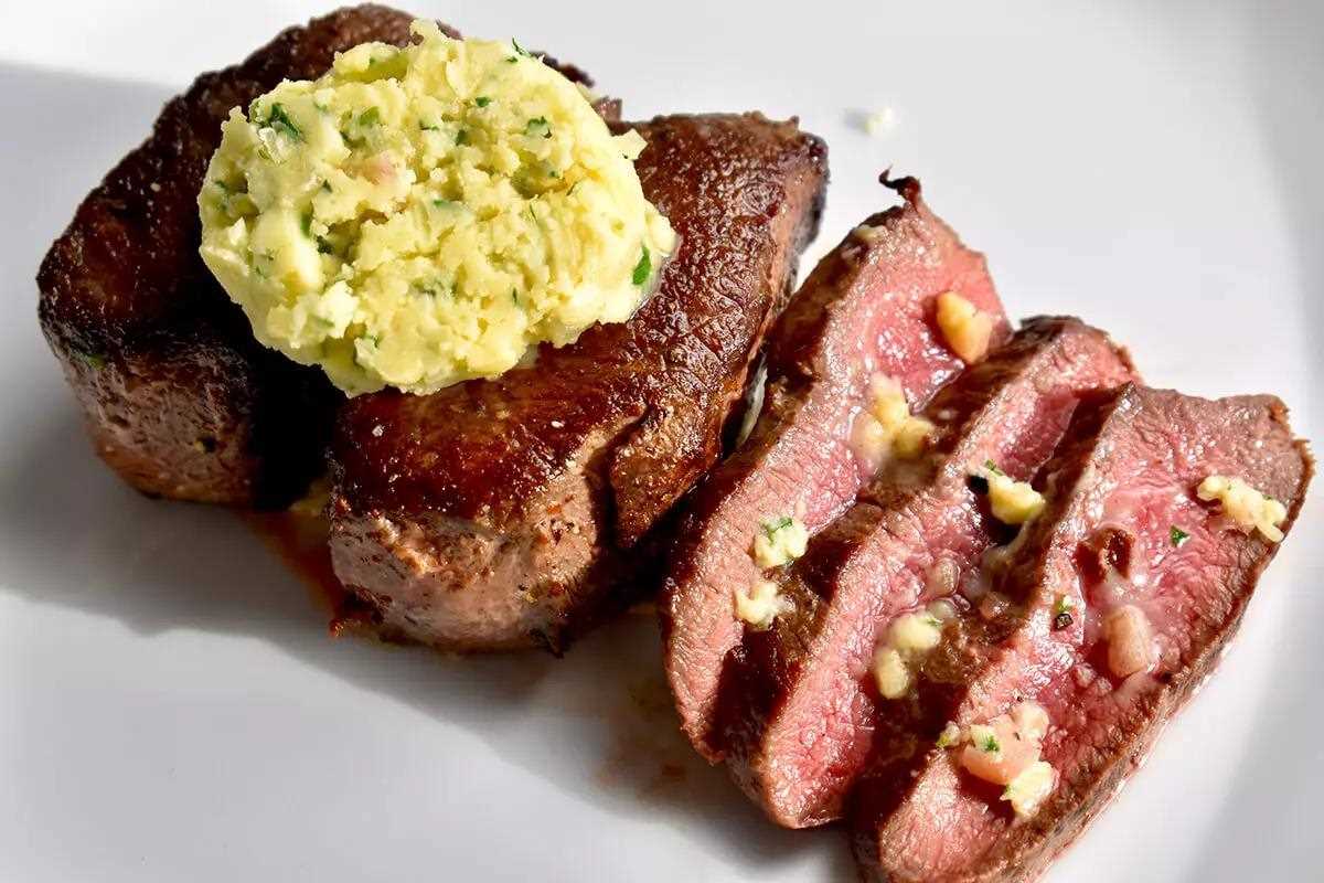 Juicy tenderloin of venison, disc of homemade bourbon button placed atop, a few slices displayed on the right with bits of butter laid across