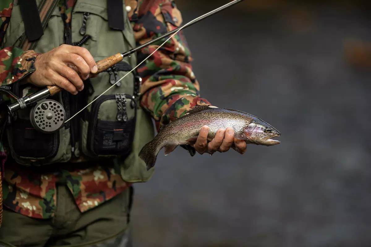 Man holding a brown spotted trout under river water while holding rod