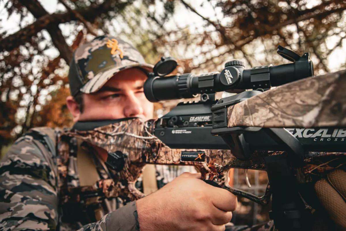 Man looking through scope of camo crossbow