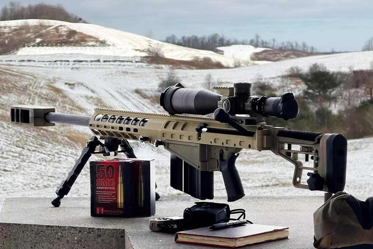 Long threaded barrel rifle with large scope on top in front of snowy hillscape