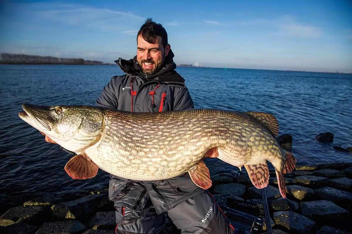 Man holding enormous giant pike over still waters