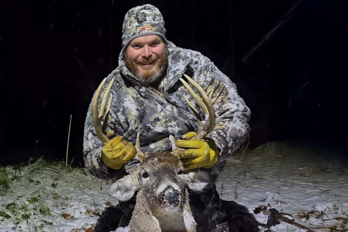 Hunter in warm camo gear holding rack of deer kill on path at night