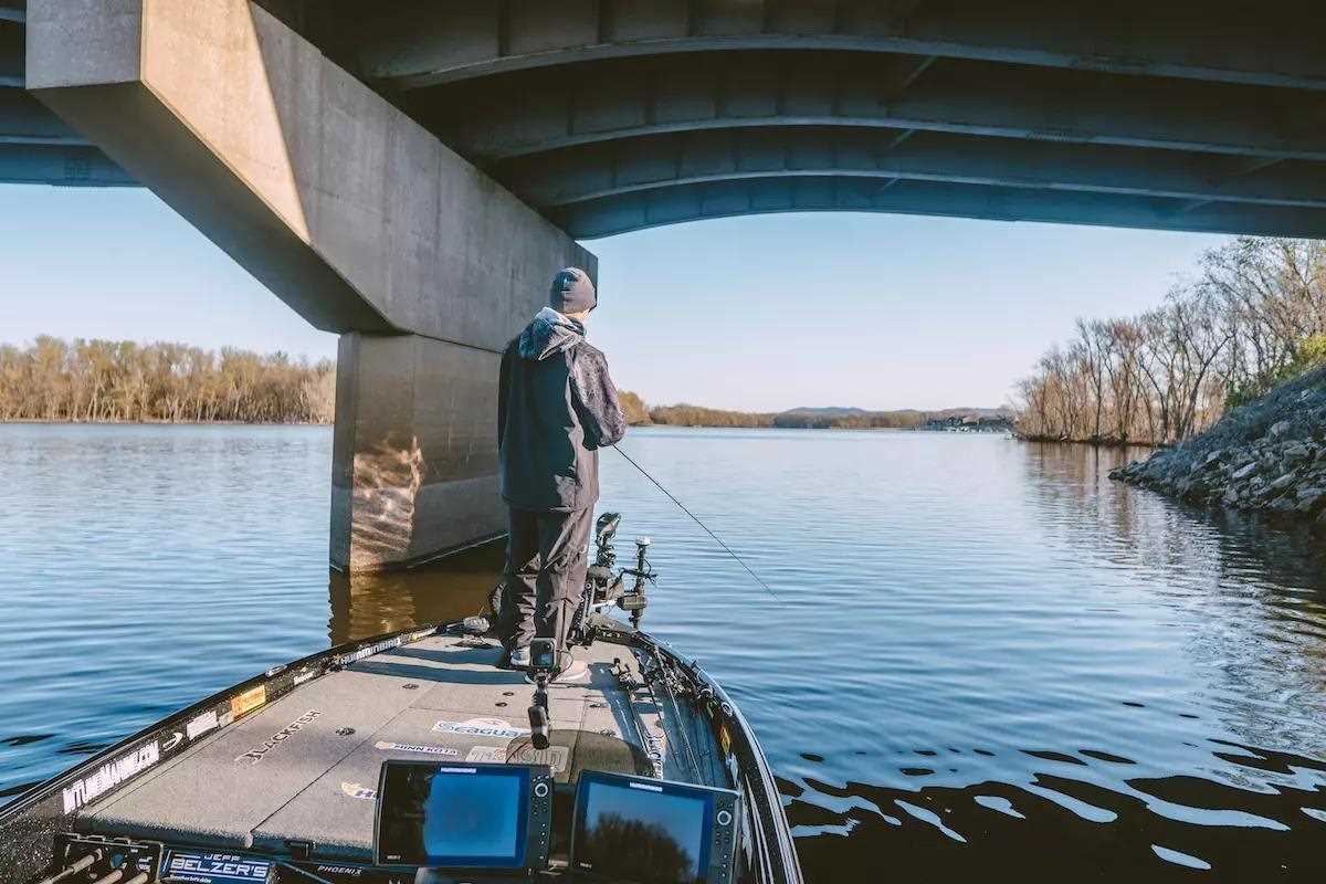 Man fishing from boat under a bridge