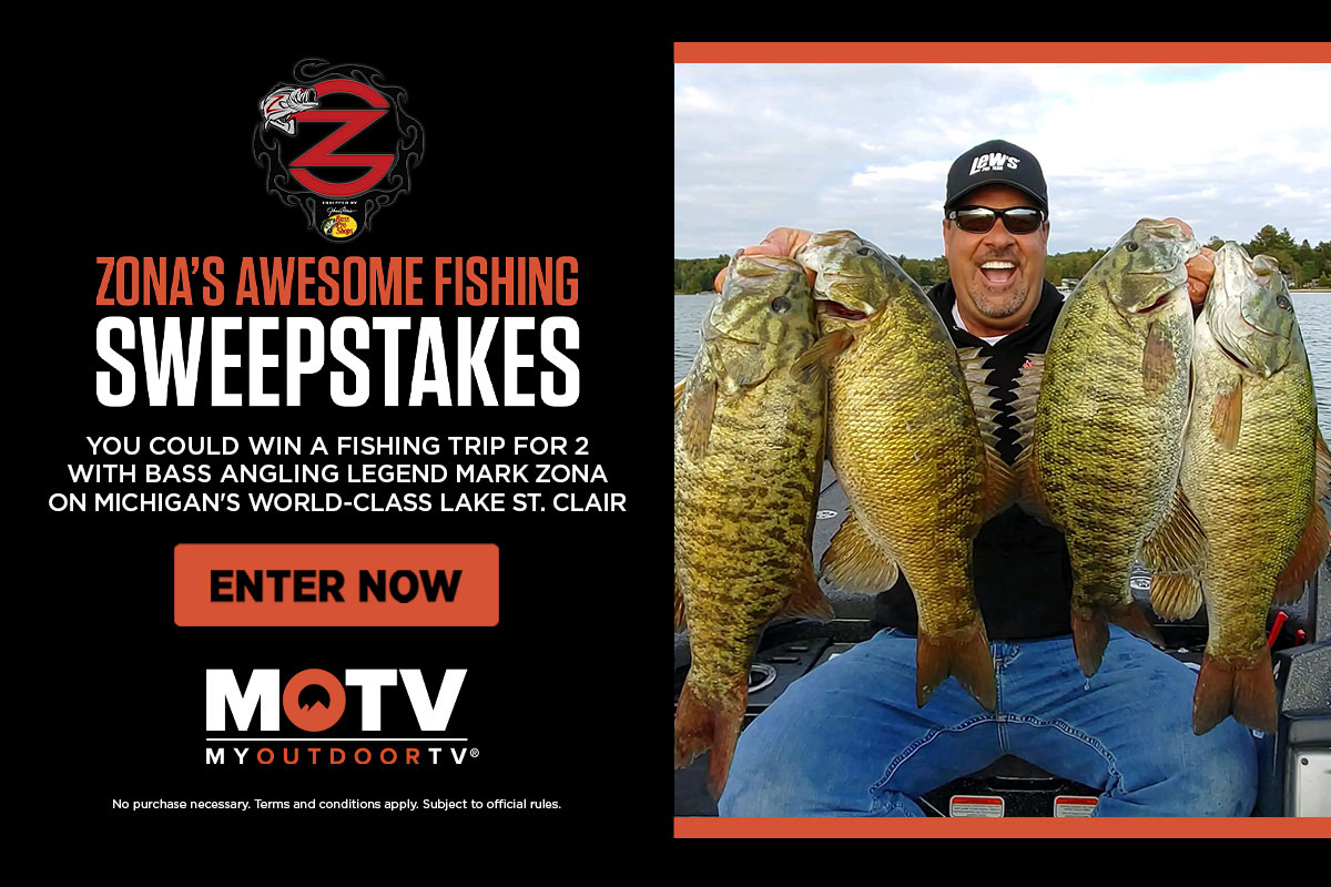 Mark Zona holding four large fish, 2 in each hand, wearing enormous smile next to water 