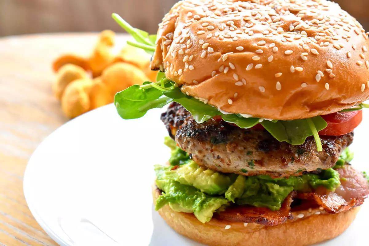 Delicious, succulent, piled-high wild turkey and chanterelle burger on a round white plate