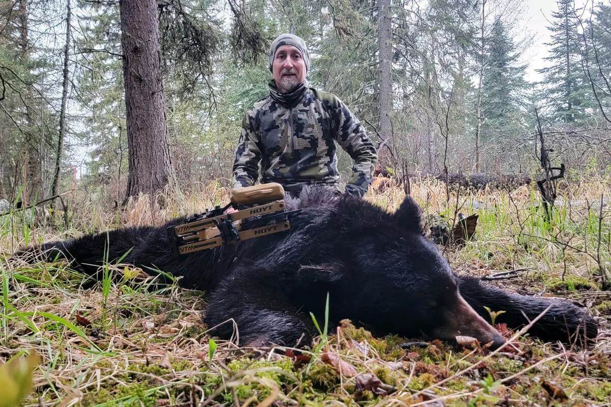Man posing over large black bear kill in woods