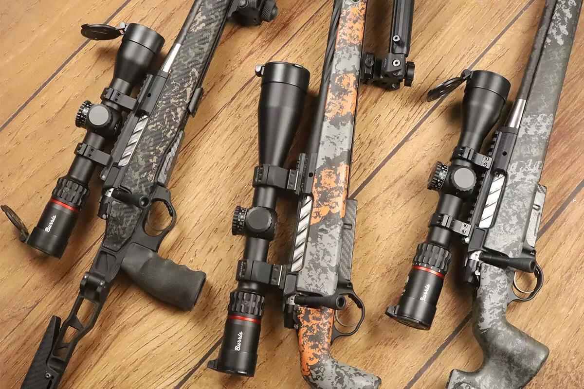 Three camouflage Burris riflescopes on a light brown wooden floor