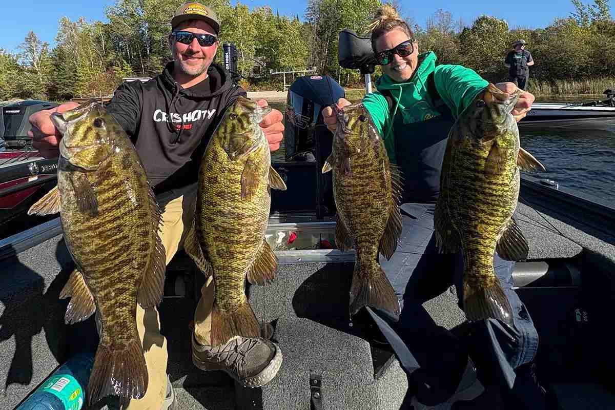 Man and woman each holding 2 large bass in boat on still waters