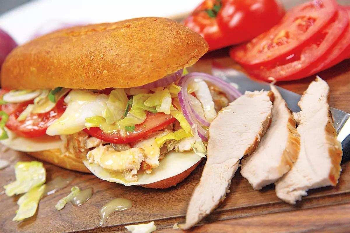 Juicy sliced turkey breast sandwich on long roll with tomato, cheese, lettuce and onion