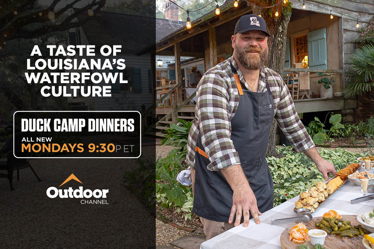 Chef at an outdoor kitchen in front of a wooden cabin 