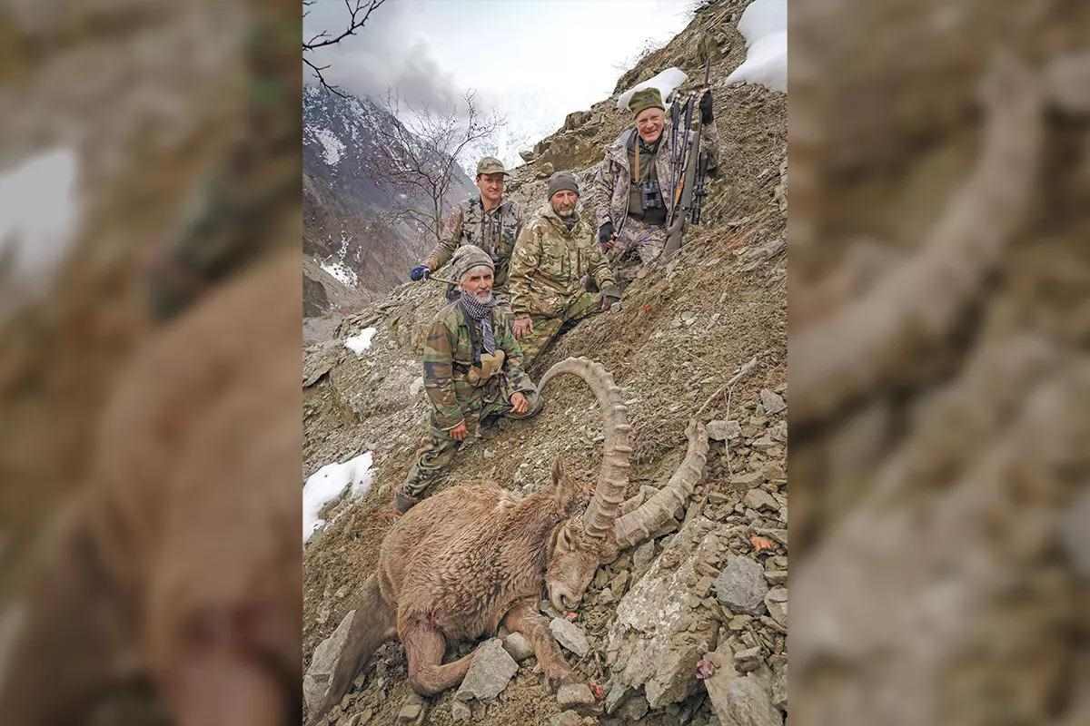 4 hunters in camo on a mountain with a downed ram in the foreground