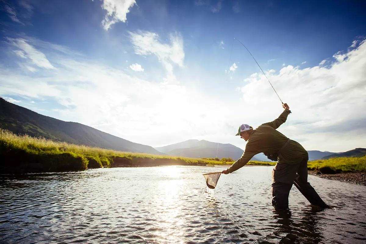 Fly fisherman casting a line in mildly active river waters with a gorgeous blue and clouded sky