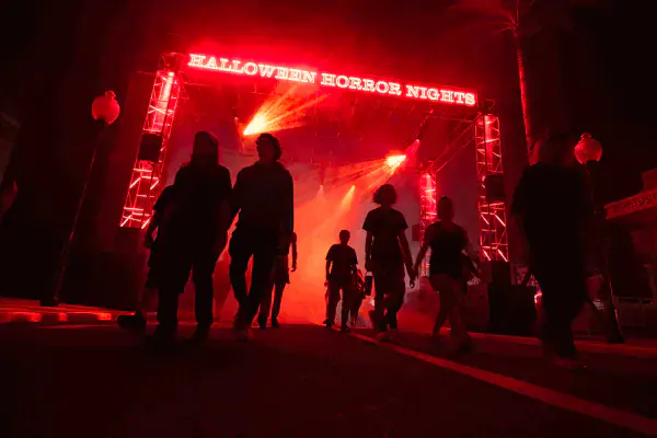 Silhouetted guests walk under a red laser light towers with the words “Halloween Horror Nights” above them at Universal Halloween Horror Nights.