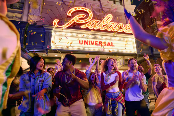A crowd of guests are watching the parade at Universal Mardi Gras: International Flavors of Carnaval. They are seen smiling and clapping in front of the Palace theater located at Universal Studios Florida.