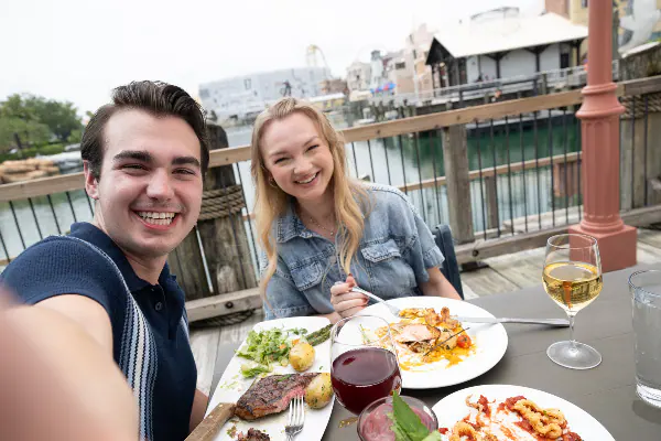 A man and woman enjoying dinner and wine at an outdoor table overlooking the water at Lombards Seafood Grill in Universal Studios Florida.