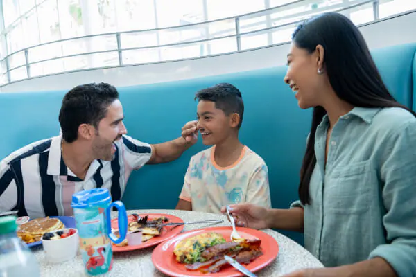 A family of three laughing and enjoying breakfast at Cabana Bay Beach Resort.
