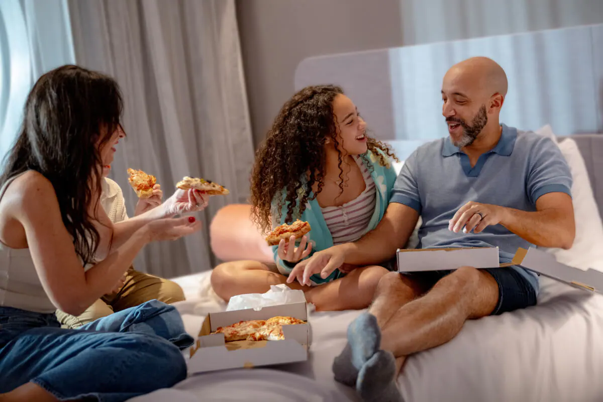 People&nbsp;A&nbsp;happy&nbsp;family&nbsp;of&nbsp;four&nbsp;laughing&nbsp;and&nbsp;eating&nbsp;pizza&nbsp;in&nbsp;their&nbsp;hotel&nbsp;room&nbsp;at&nbsp;Stella&nbsp;Nova&nbsp;Resort.