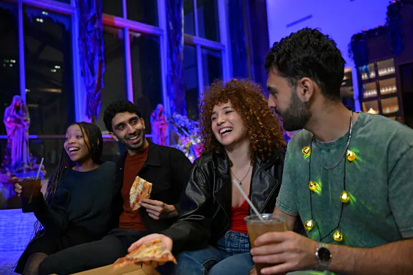 A group of four friends laughing and enjoying pizza at Cabana Bay’s Swizzle Lounge during Halloween Horror Nights.
